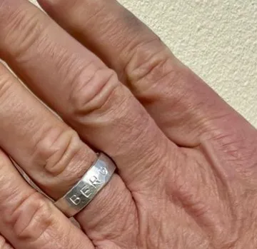 Hand trägt silbernen Ring mit Gravur.