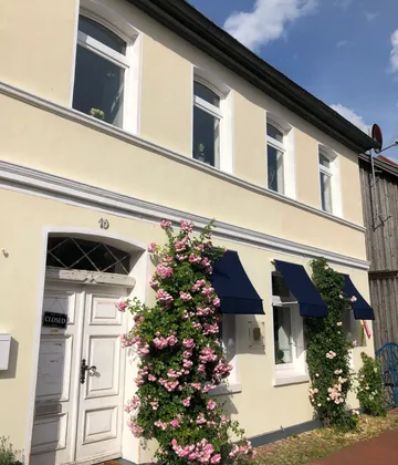 House with flowers, blue awnings, closed door.