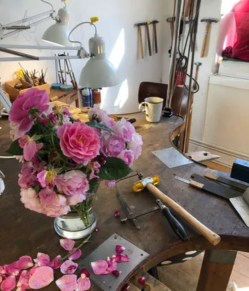 Rosa Rosen in Vase auf unordentlicher Werkbank.