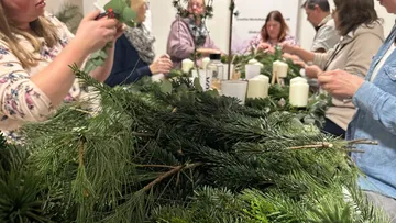 Menschen basteln Kränze an einem Tisch.