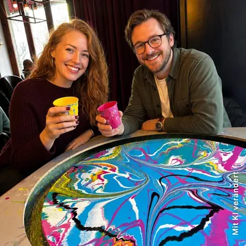 Two people hold colorful cups indoors.
