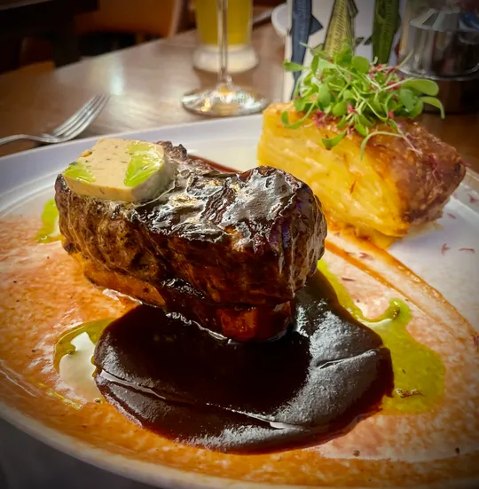 Steak mit Sauce auf weißem Teller, Restaurantumgebung.