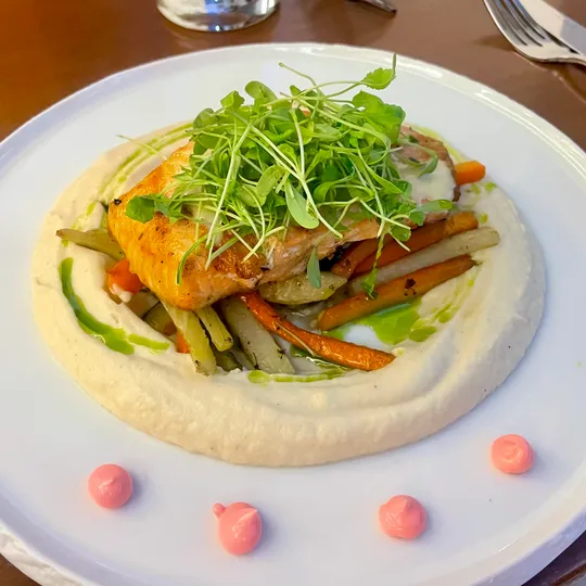 Lachs auf Gemüse mit Microgreens auf Teller serviert.