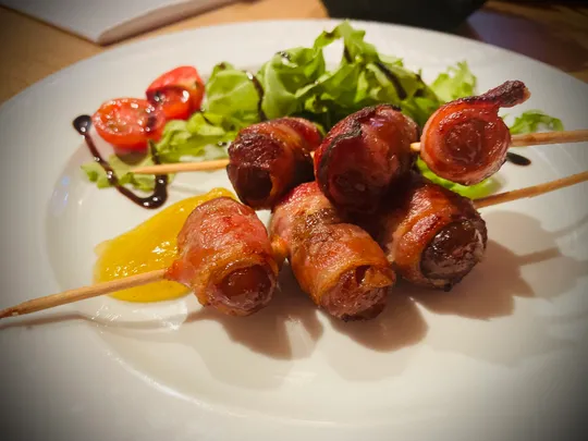 Speckumwickelte Würstchen auf Spießen mit Salatgarnitur.