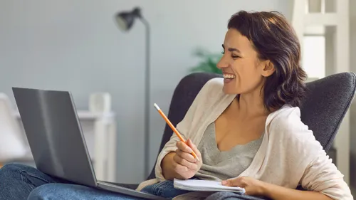 Frau lächelt beim Laptopbenutzen, sitzt im Sessel.