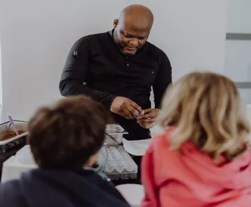 Koch bereitet Essen zu, zwei Kinder schauen zu.
