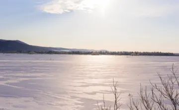 Gefrorener See reflektiert Sonnenlicht, Berge im Hintergrund.