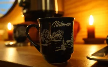 Tasse mit Glühwein-Text, Kerzen, Holzhintergrund.