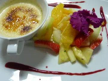 Crème brûlée and fresh fruit salad on a white plate.