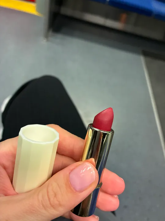 Person holding lipstick on public transport.