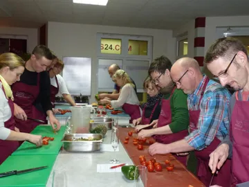 Chefs cut tomatoes in a cooking school with tables.
