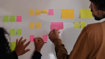 Personen ordnen bunte Haftnotizen an Tafel an.