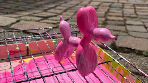 Pink balloon dog on metal grid outdoors.