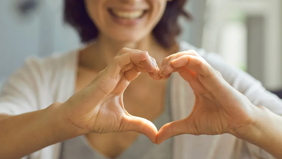 Hands forming heart shape, smiling face visible.