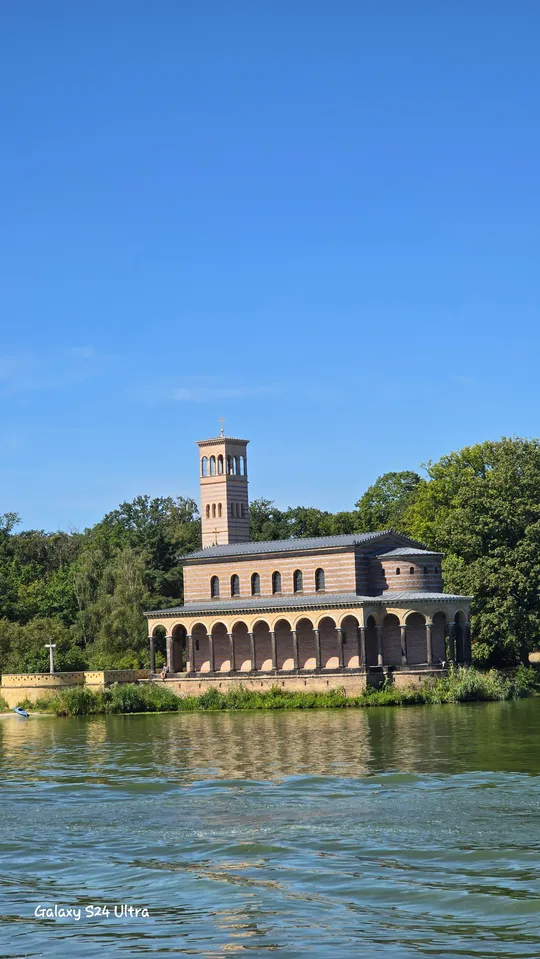 Church with tower beside river, trees around.