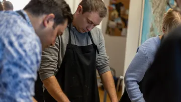 Menschen in Schürzen kochen in einer Küche.