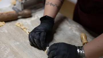 Hands wearing gloves making pasta on table.