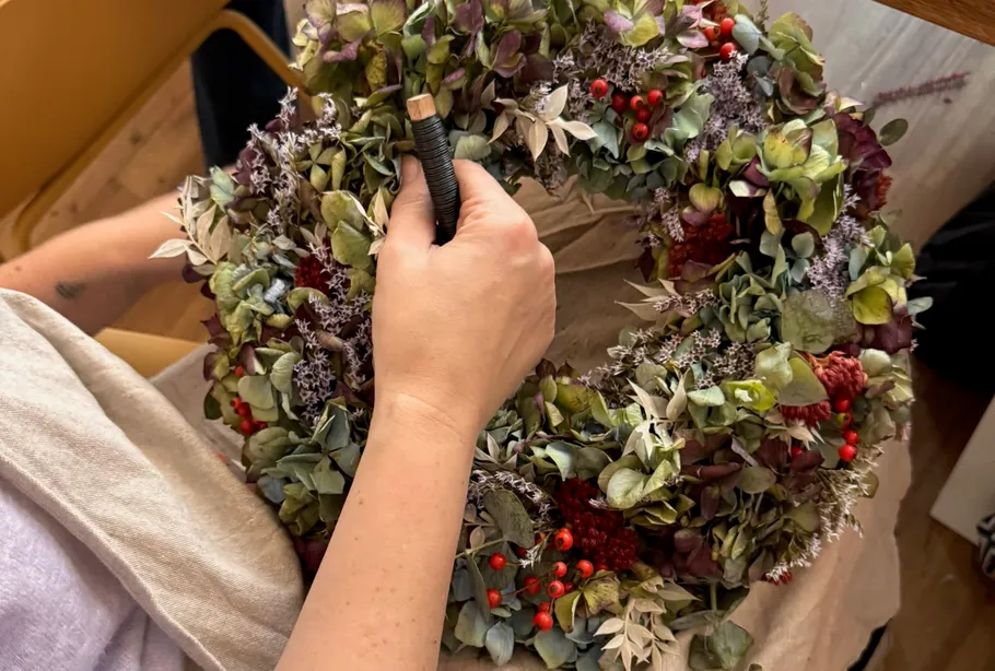 Hands creating floral wreath on table.