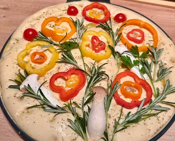 Dough topped with peppers and herbs on table.