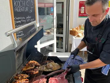Grilling chef serving meat and side dishes outdoors.