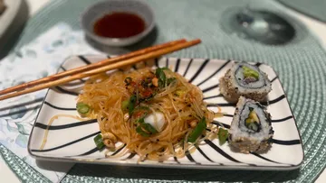 Noodles and sushi on a black-striped plate.