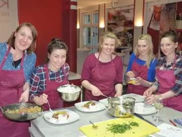 Six women cook together in a modern kitchen.