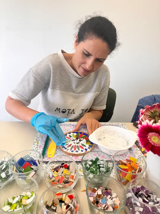 Frau erstellt Mosaikkunst mit bunten Fliesen.