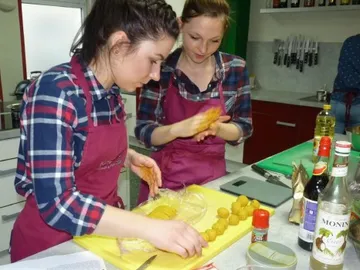Two women make dough balls in a modern kitchen.