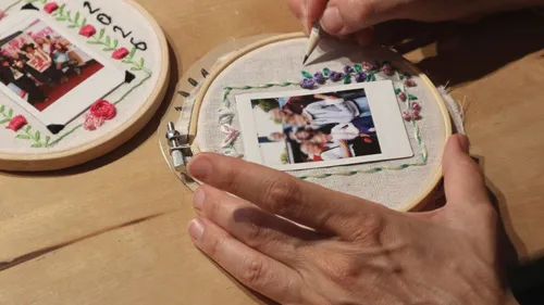 Hands embroidering photo on wooden table.