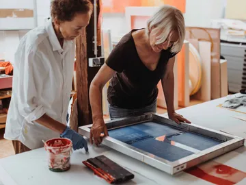 Two women work together on a print frame.