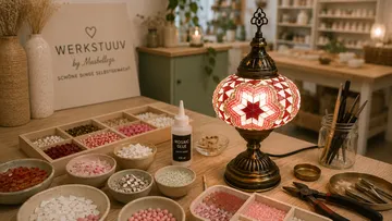 Mosaiklampe leuchtet auf Basteltisch mit Material.