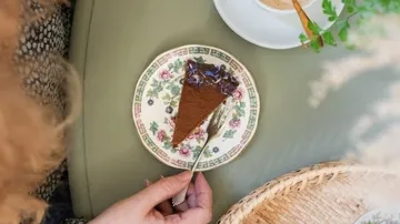 Slice of cake on floral plate, coffee nearby.