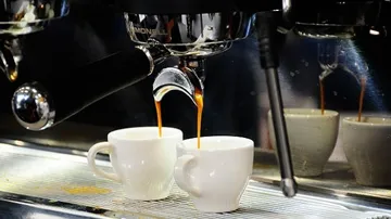 Espressomaschine füllt Kaffee in Tassen.