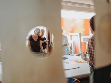 Three women look at works of art in a studio.