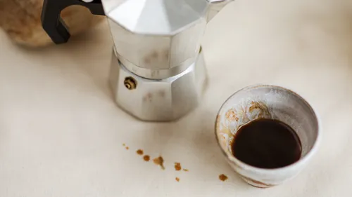 Espresso maker beside a small cup on table.