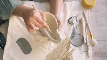 Hände formen Ton mit Werkzeugen daneben.