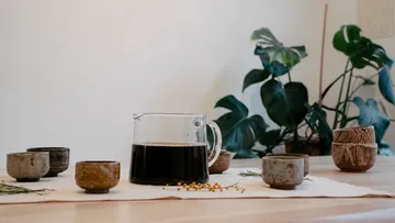 Keramikbecher und Kaffeekanne auf Tisch.