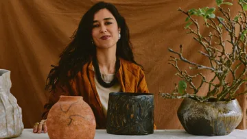 Woman seated with pottery and plant.