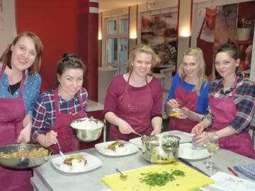 Five women prepare dishes in a modern cooking school.