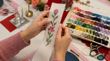 Hände halten bestickten Stoff mit Blumen.