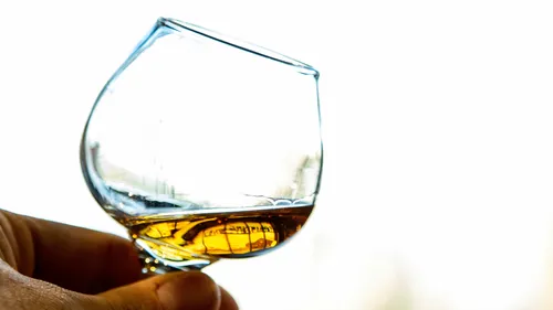 Hand holding glass with amber liquid.