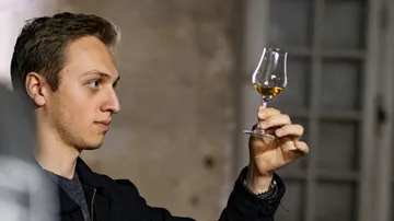 Person examines whiskey glass indoors.
