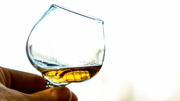 Hand hält Glas mit brauner Flüssigkeit.