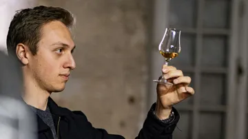 Mann inspiziert bernsteinfarbene Flüssigkeit im Glas drinnen.