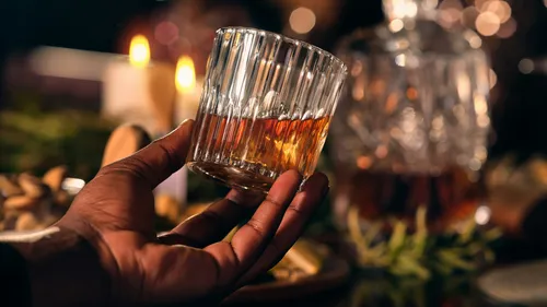 Hand hält Whiskyglas, beleuchtete Essensszene.