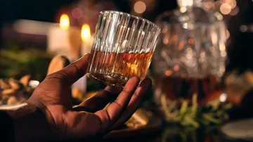 Hand hält Whiskyglas, Kerzenhintergrund.