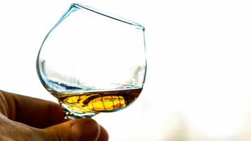 Hand holding tilted glass of whiskey.