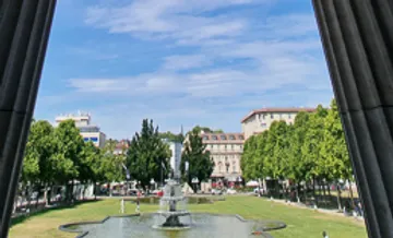 Brunnen im Park, umgeben von Bäumen, Gebäuden.
