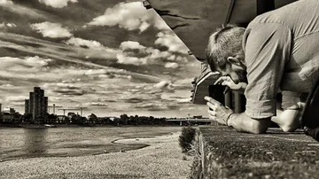 Person photographing riverfront cityscape with cellphone.