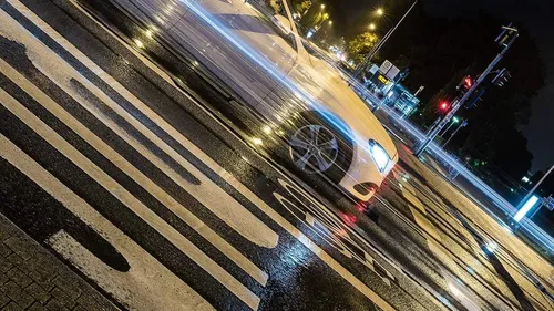 Car speeding through wet street at night.